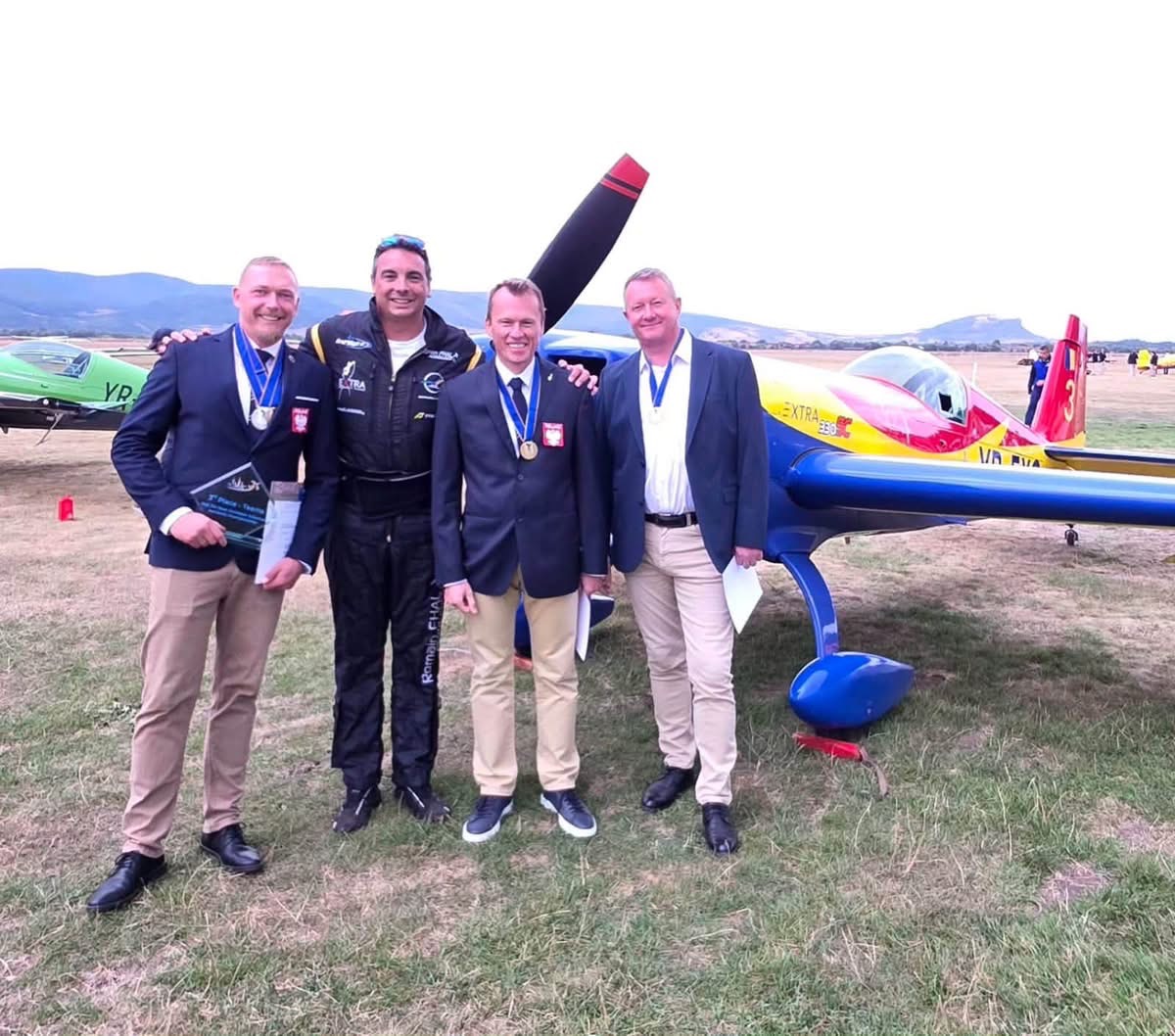 Polscy zawodnicy z medalami i trener Romain Fhal przy Extra 330SC na lotnisku w Deva